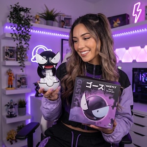 Pode incluir: Uma figura do Gastly emergindo de uma Poké Ball branca e preta, segurada ao lado da sua caixa de embalagem quadrada. A caixa apresenta a personagem Gastly, o texto japonês ゴース e o texto em inglês GASTLY Ghost buryie gas em branco e preto.