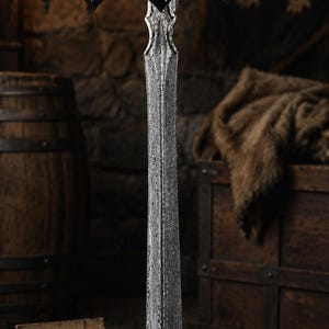 May include: A double-edged sword with a patterned Damascus steel blade, a black hilt with silver-colored accents, and a crossguard featuring white line engravings. A wooden sign with the text Blade Legacy Forge is positioned at the base.