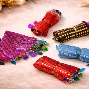 Puede incluir: Una variedad de artículos decorativos coloridos. Los artículos incluyen cilindros rojos, azules y negros con lunares dorados o blancos y lentejuelas. Algunos están envueltos con hilo dorado y adornados con hojas decorativas y detalles morados.