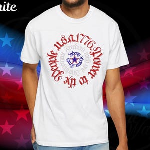 May include: White t-shirt with a patriotic design. The design features the text "USA 1776" in red, encircling a blue star and the words "Freedom, Liberty, Power, With, Our, Strength, To, The, People".