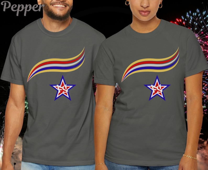 May include: Two gray t-shirts with a star and ribbon design. The star is blue with a red and white outline and a red design in the center. The ribbon is yellow, red, and blue. The shirts are short-sleeved.