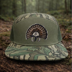 Op de afbeelding: Groene en camouflage truckerpet met een kalkoen-embleem. De pet heeft een mesh achterkant, een platte klep en een patch met een gedetailleerd geborduurd kalkoenontwerp. Ontworpen voor outdoorliefhebbers.