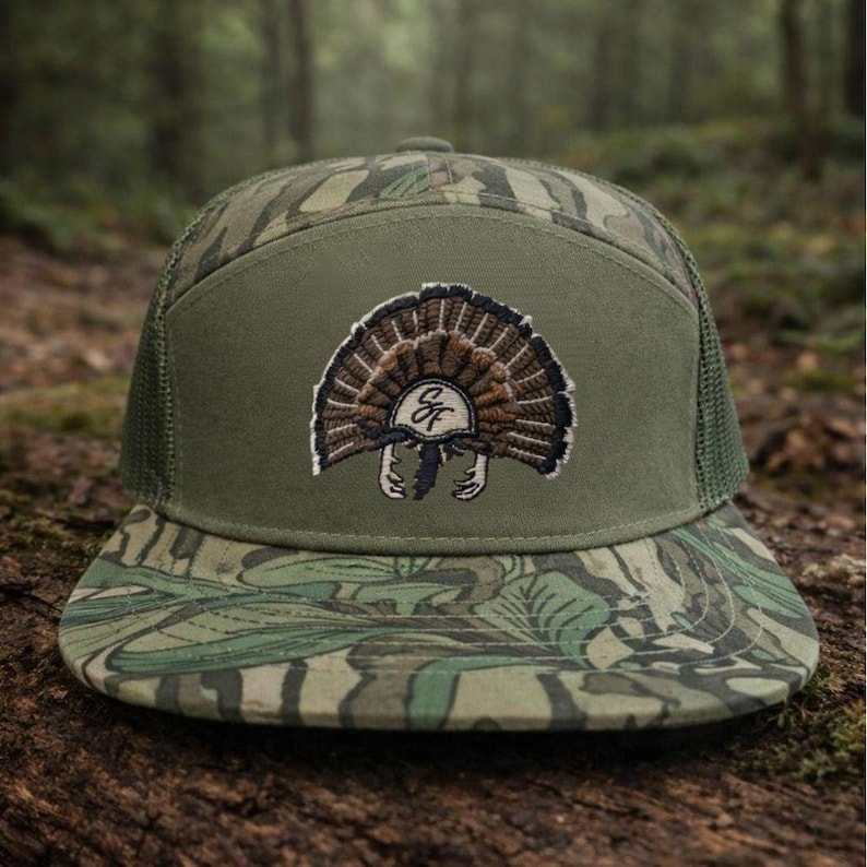 Op de afbeelding: Groene en camouflage truckerpet met een kalkoen-embleem. De pet heeft een mesh achterkant, een platte klep en een patch met een gedetailleerd geborduurd kalkoenontwerp. Ontworpen voor outdoorliefhebbers.