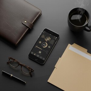 May include: A professional workspace featuring a brown leather bound notebook, a smartphone displaying a law-themed app, a cup of coffee, eyeglasses, a pen, and file folders. The items are arranged on a dark surface.