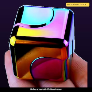 May include: A holographic edition cube-shaped fidget toy with a chrome finish. The cube reflects a rainbow of colors, including blue, yellow, and pink. The text "HOLOGRAPHIC EDITION" is visible on the top right. The bottom of the image has the text "Reflets arc-en-ciel • Finition chromée."