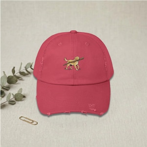 Puede incluir: Gorra de béisbol roja desgastada con una imagen bordada de un golden retriever llevando un palo. La gorra tiene una visera curva y un aspecto vintage desgastado, para amantes de los perros.