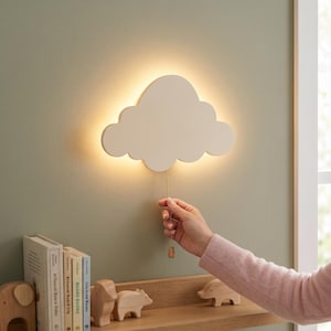 May include: A cloud-shaped wall lamp with a smooth, matte finish emits a warm, soft glow from behind its edges. A thin, metallic pull chain hangs from the center of the bottom edge, allowing for manual operation of the light fixture.