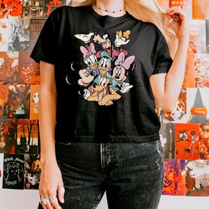 May include: Black t-shirt featuring a colorful graphic of Disney characters including Mickey Mouse, Minnie Mouse, Donald Duck, Daisy Duck, Goofy, and Pluto. The shirt is a classic crew neck style.