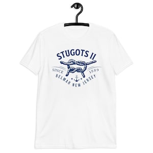 May include: White t-shirt with a navy blue nautical design featuring the text "STUGOTS II" above a rope knot, the words "SINCE BELMAR NEW JERSEY 1889" and an anchor. The shirt is hanging on a black hanger.