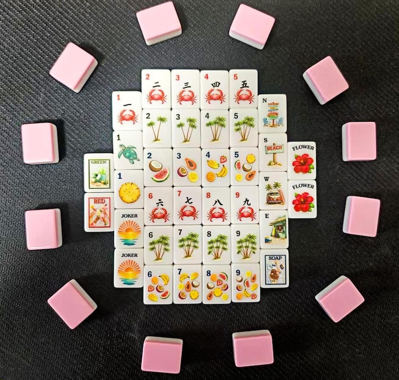 Puede incluir: Un juego completo de Mahjong con fichas blancas que presentan varios s&iacute;mbolos, n&uacute;meros y caracteres, incluidos cangrejos, palmeras y frutas. Las fichas rosas est&aacute;n dispuestas alrededor de las piezas del juego. El juego est&aacute; sobre una superficie oscura.