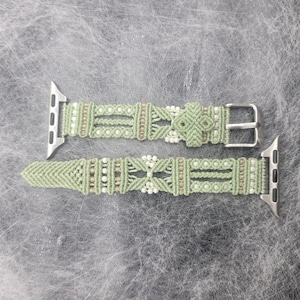 Op de afbeelding: Een lichtgroene macramé Apple Watch band. De band heeft een geweven ontwerp met kleine witte en bruine kralen. Het heeft zilverkleurige metalen connectoren en een gesp.