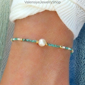 May include: A delicate bracelet with turquoise, white, and gold beads. A central, large pearl is set in gold-coloured metal. The bracelet is strung on a thin cord, creating a minimalist and elegant design. The bracelet is a stylish piece of jewellery.