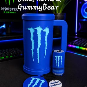 May include: A blue mug featuring the Monster Energy logo, a small blue can-shaped keychain with the same logo, and a round blue coaster with the logo and a white tag reading WebsHouse Creations.com. Text above reads BluePhoria & GummyBear.