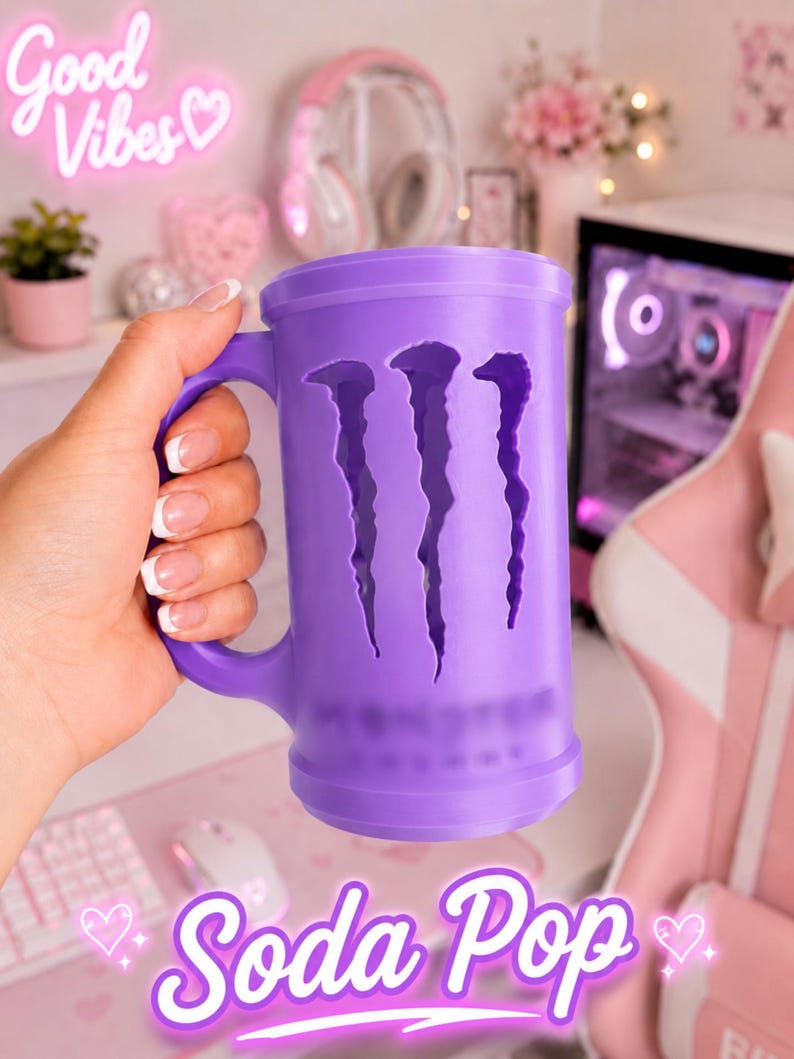 May include: A purple cylindrical mug featuring a cutout of the Monster Energy logo on the front. The mug has a sturdy handle on the side and a smooth, matte finish. The design includes a recessed area where the iconic claw mark graphic is visible.