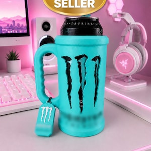 Puede incluir: Un portabebidas de color turquesa brillante con forma de jarra y asa. El soporte presenta un recorte del logotipo de Monster Energy, que revela una lata negra en su interior. Una pequeña etiqueta turquesa a juego con el logo blanco cuelga del asa.