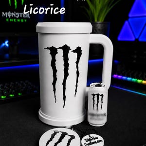 May include: A white mug featuring a large black Monster Energy logo, accompanied by a miniature white can replica and a round white keychain with the same logo and the text WebPlane Creations.com, labeled Coconut & Black Licorice.