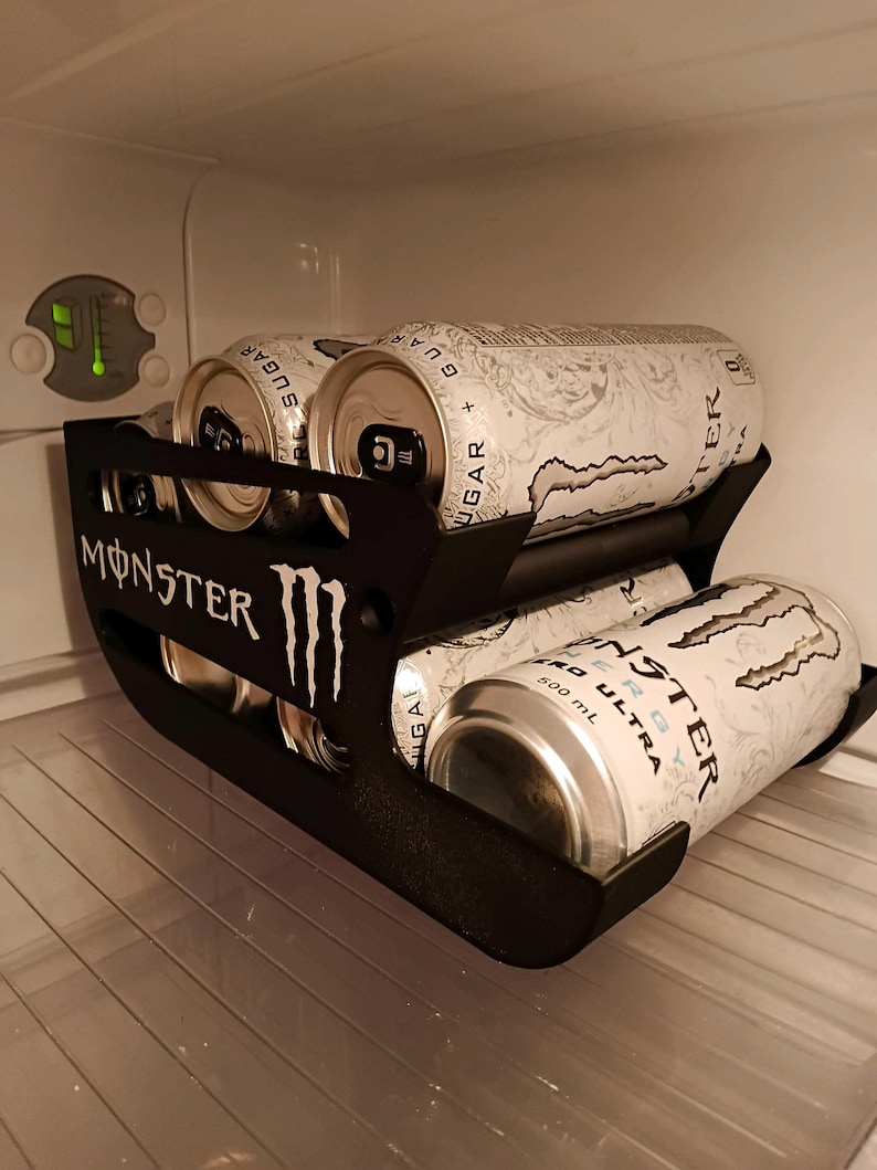 May include: A black plastic beverage can organizer rack featuring the Monster Energy logo on the side. The rack holds multiple white Monster Energy Zero Ultra cans, each labeled 500 mL, arranged in two tiers within a refrigerator interior.
