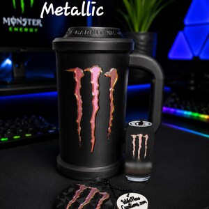 May include: A matte black mug featuring a metallic Monster Energy logo, accompanied by a matching small canister and a circular keychain with the same logo and the text "WifePleas Creations.com". The text "Black Licorice & Metallic" is visible.