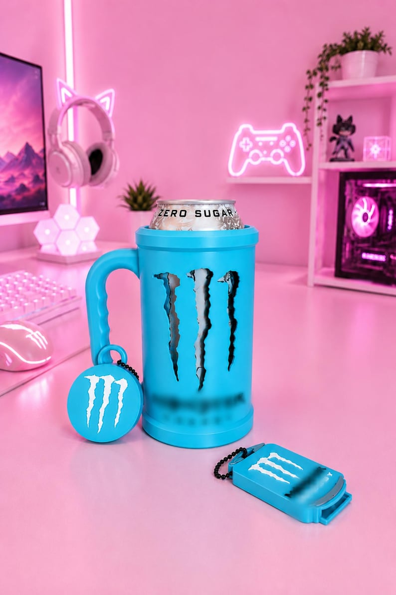 May include: A bright blue cylindrical beverage holder with a handle, featuring a black claw mark graphic and the Monster logo. A silver can labeled Zero Sugar is inserted inside. A circular tag and a rectangular tag with the logo are attached.