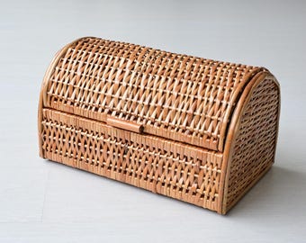Könnte beinhalten: Ein rechteckiger Brotkasten aus hellbraunem Korbgeflecht mit einem gewölbten Klappdeckel. Der geflochtene Korb weist ein enges, gleichmäßiges Gittermuster am gesamten Körper und Deckel auf, mit einem kleinen Holzgriff mittig an der Vorderkante.