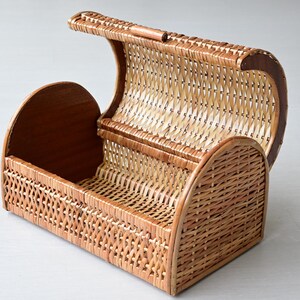 May include: A rectangular wicker basket with a rounded, hinged lid that opens upward. The basket features a woven light brown reed pattern on the sides and lid, complemented by solid, smooth wooden end panels and a matching wooden handle on top.