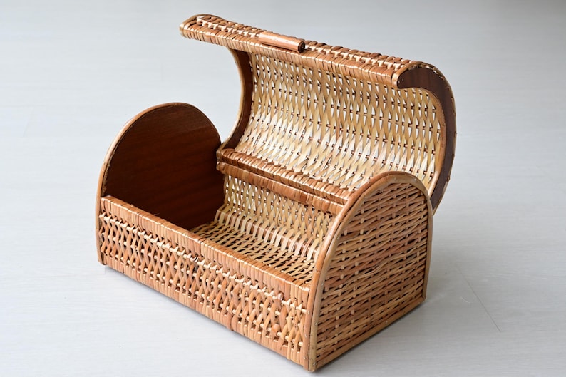 May include: A rectangular wicker basket with a rounded, hinged lid that opens upward. The basket features a woven light brown reed pattern on the sides and lid, complemented by solid, smooth wooden end panels and a matching wooden handle on top.