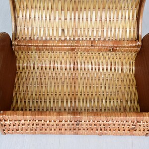 May include: A light brown woven wicker basket with a semi-cylindrical shape and a hinged lid. The basket features a natural tan finish with darker brown solid wood side panels, showcasing a detailed interlaced pattern throughout the structure.