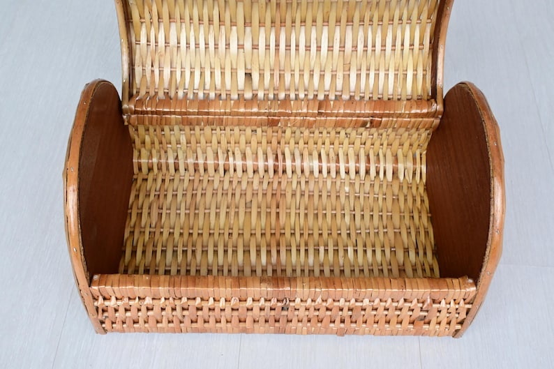 May include: A light brown woven wicker basket with a semi-cylindrical shape and a hinged lid. The basket features a natural tan finish with darker brown solid wood side panels, showcasing a detailed interlaced pattern throughout the structure.