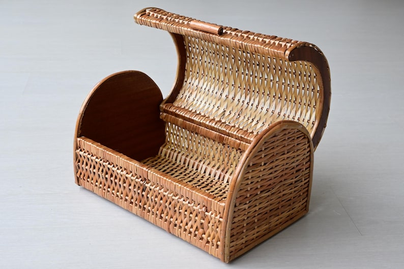 May include: A rectangular woven wicker basket featuring a hinged, arched lid that opens upward. The basket is constructed from light brown natural reeds with a cross-weave pattern on the sides and a solid wooden base and side panels.