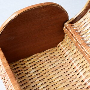 May include: A woven wicker basket featuring a light tan natural finish and a solid, smooth, dark brown wooden end panel. The basket has a curved, open-top design with a structured frame, showcasing a detailed crisscross weave pattern throughout.