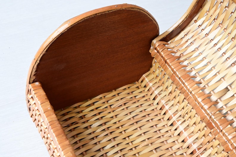 May include: A woven wicker basket featuring a light tan natural finish and a solid, smooth, dark brown wooden end panel. The basket has a curved, open-top design with a structured frame, showcasing a detailed crisscross weave pattern throughout.