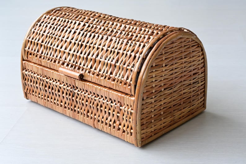 May include: A rectangular wicker basket with a rounded, arched lid. The basket is constructed from light brown woven reeds in a cross-hatch pattern. It features a hinged top cover that extends over the front, secured by a small horizontal latch.