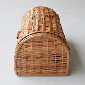 May include: A light brown woven wicker bread box with a semi-cylindrical arched top and a rectangular base. The basket features a horizontal weave pattern throughout, with a small wooden handle attached to the side for opening the curved lid.