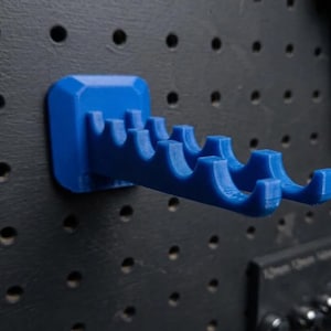 May include: A bright blue pegboard tool holder. The holder is designed to attach to a pegboard and features multiple curved slots for organizing tools. The holder is made of a solid, durable material.