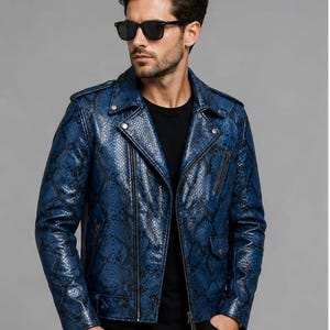 May include: A blue and black snakeskin-patterned motorcycle jacket featuring a notched lapel, silver-tone metal zippers, a diagonal front closure, shoulder epaulets, and a small flap pocket on the lower front, worn over a plain black shirt.
