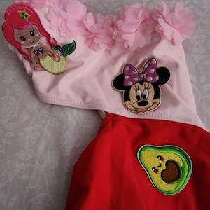 May include: A pink and red swimsuit with appliqued designs. The top is pink with pink flower accents and a mermaid applique. The bottom is red with an avocado applique and a Minnie Mouse applique.