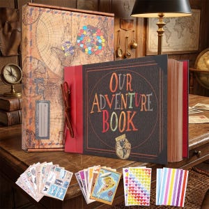May include: An adventure-themed scrapbook with the words "Our Adventure Book" on the cover. The cover is dark brown with colorful lettering. A matching box with a world map design and stickers are also included.