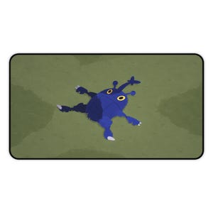 Pode incluir: Um tapete de rato azul e preto com uma criatura de desenho animado com olhos e antenas amarelas. A criatura está deitada sobre um fundo verde. O tapete tem uma borda preta.