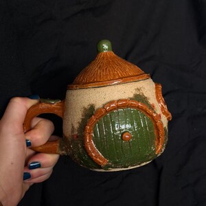 Mug en grès fait main représentant une maison de hobbit avec couvercle, poterie fantastique et chaleureuse, chope à bière en céramique aux tons verts et bruns.