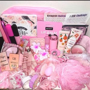 Könnte beinhalten: Eine rosa Geschenkbox voller Beauty- und Schreibwarenartikel. Enthält Lippenbalsam, Handcreme, Make-up, Bleistifte, ein Notizbuch und dekorative Blumen. Die Box enthält auch kleine Geschenktüten und einen rosa Badeschwamm.
