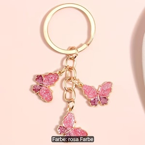 Puede incluir: Un llavero de metal dorado con tres dijes de mariposa colgantes. Cada mariposa est&aacute; decorada con un acabado degradado brillante en rosa y magenta. El llavero incluye una argolla circular unida a una cadena corta con las mariposas.