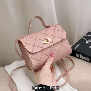 Puede incluir: Un bolso de mano rosa claro con un patr&oacute;n de diamantes acolchado en el exterior. El bolso incluye un asa superior, una correa fina para el hombro y un cierre giratorio de metal dorado en la solapa frontal. El texto "Farbe: rosa Farbe" es visible.