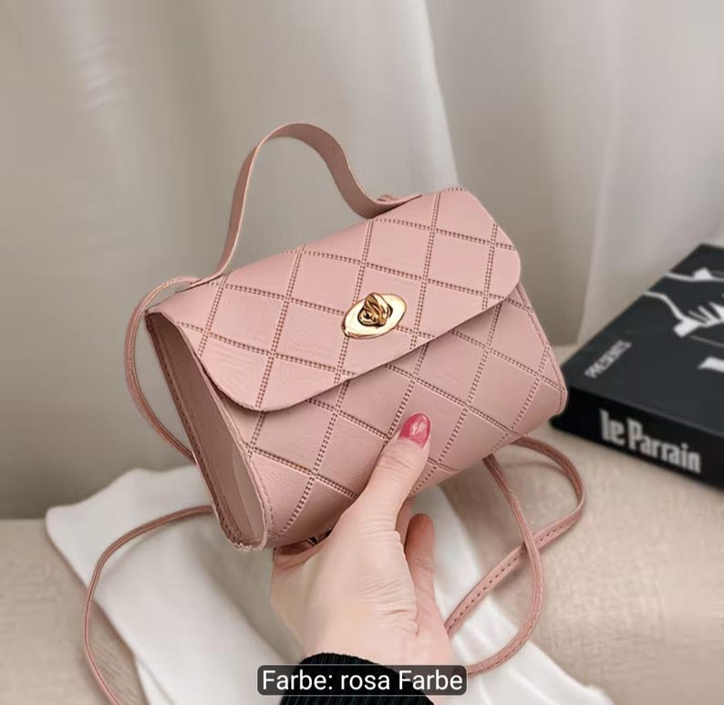 Puede incluir: Un bolso de mano rosa claro con un patr&oacute;n de diamantes acolchado en el exterior. El bolso incluye un asa superior, una correa fina para el hombro y un cierre giratorio de metal dorado en la solapa frontal. El texto "Farbe: rosa Farbe" es visible.