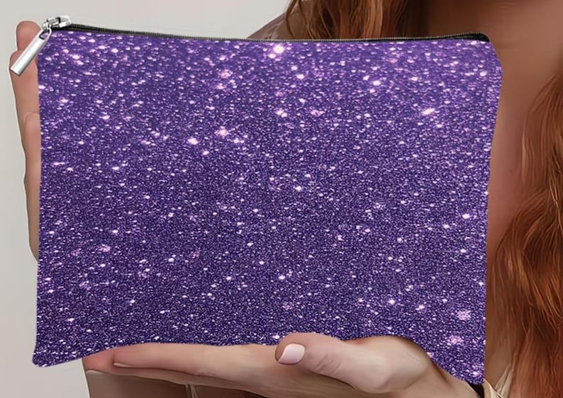 Puede incluir: Un estuche rectangular con cremallera que presenta un acabado de purpurina morada en toda la superficie. El exterior muestra una textura densa y brillante con numerosas part&iacute;culas que reflejan la luz, creando un efecto centelleante. Un tirador de cremallera de metal plateado est&aacute; sujeto en la esquina superior.