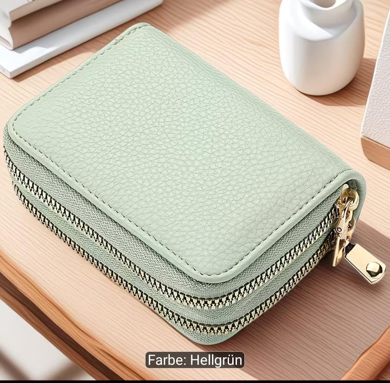 Puede incluir: Una cartera rectangular de color verde menta con una superficie texturizada y esquinas redondeadas. La cartera cuenta con dos compartimentos con cremalleras met&aacute;licas en tono dorado y tiradores a juego para un cierre seguro.