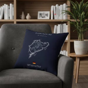 Peut inclure: Un coussin bleu marine avec un contour blanc du circuit de Nürburgring, avec le texte "Nürburgring The Green Hell". Le coussin comprend également le drapeau allemand et les détails de la piste.