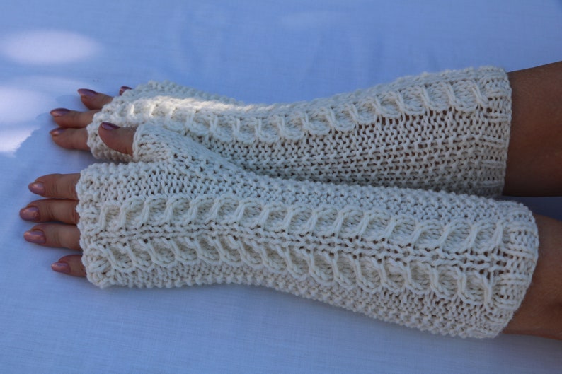 May include: A pair of white knitted fingerless gloves with a cable knit pattern.