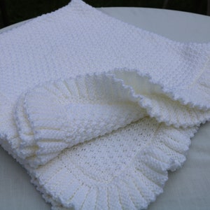 May include: A white crocheted baby blanket with a ruffled edge.