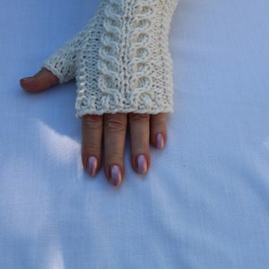 May include: White knitted fingerless gloves with a cable knit pattern.
