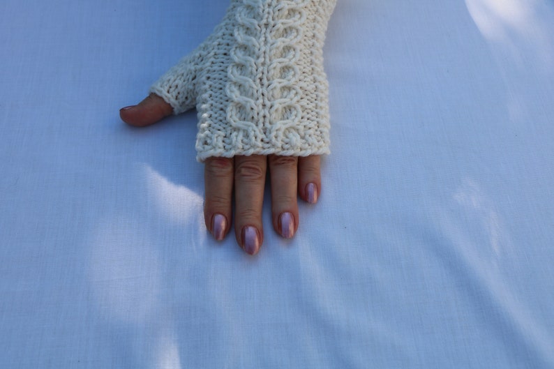 May include: White knitted fingerless gloves with a cable knit pattern.